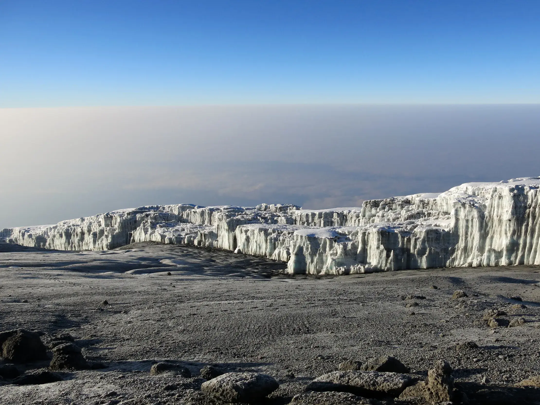 Die beeindruckende Gletscherwand am Uhuru Peak, dem Gipfel des Kilimanjaro, ragt aus der kargen Hochebene über den Wolken.