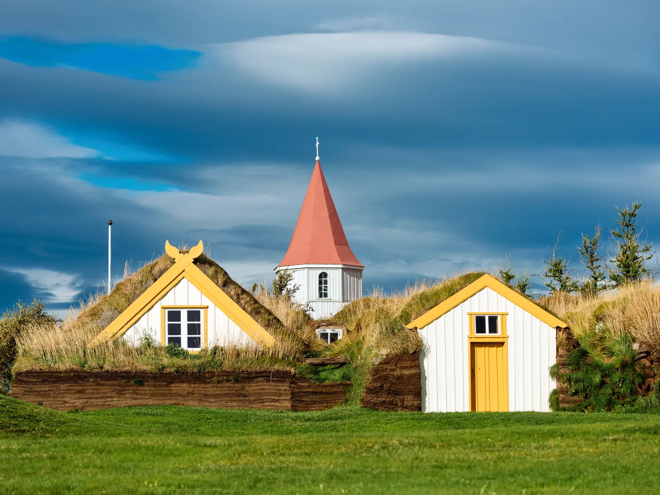 Die traditionelle Torfkirche Vidimyri in Island mit ihren grasbedeckten Torfhäusern unter einem dramatischen Himmel.