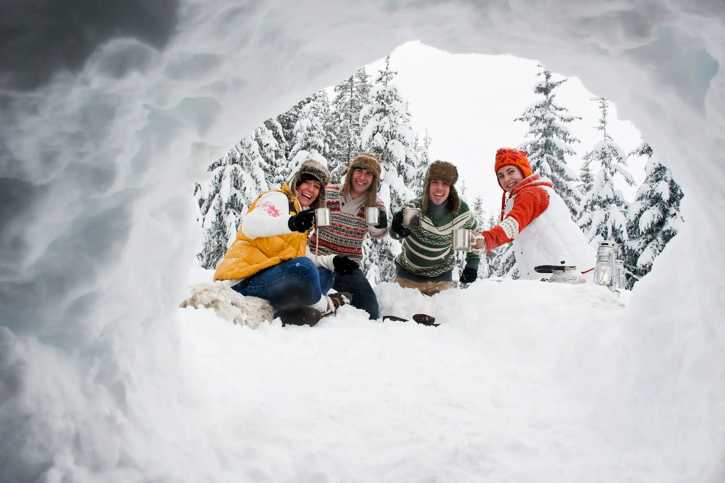 Eine fröhliche Gruppe junger Leute prostet sich mit Tassen zu, fotografiert aus einem Iglu in der verschneiten Waldlandschaft Finnlands.