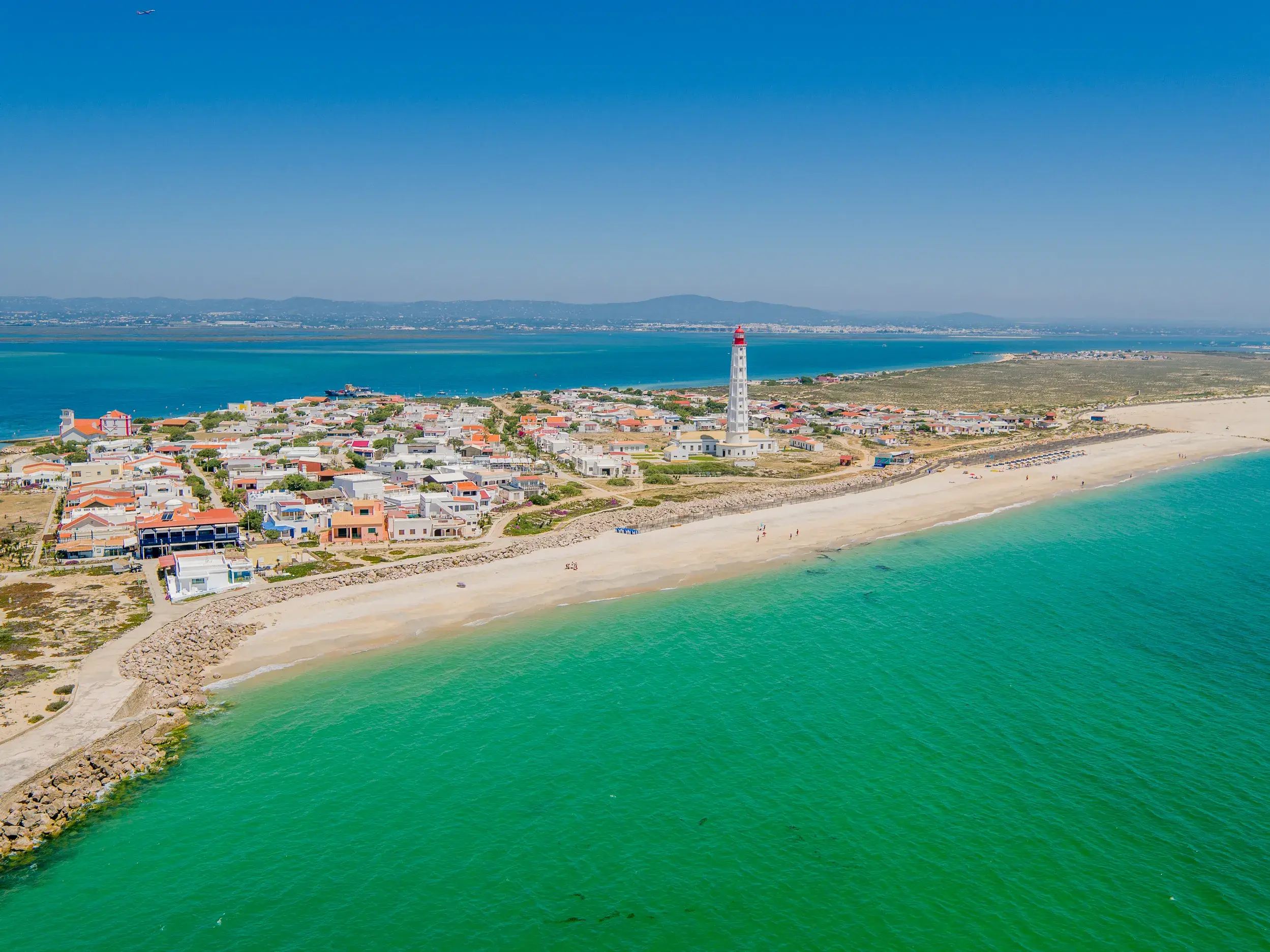 Blick auf den Leuchtturm von Farol und den Sandstrand auf der Insel Culatra im Naturpark Ria Formosa an der Algarve.