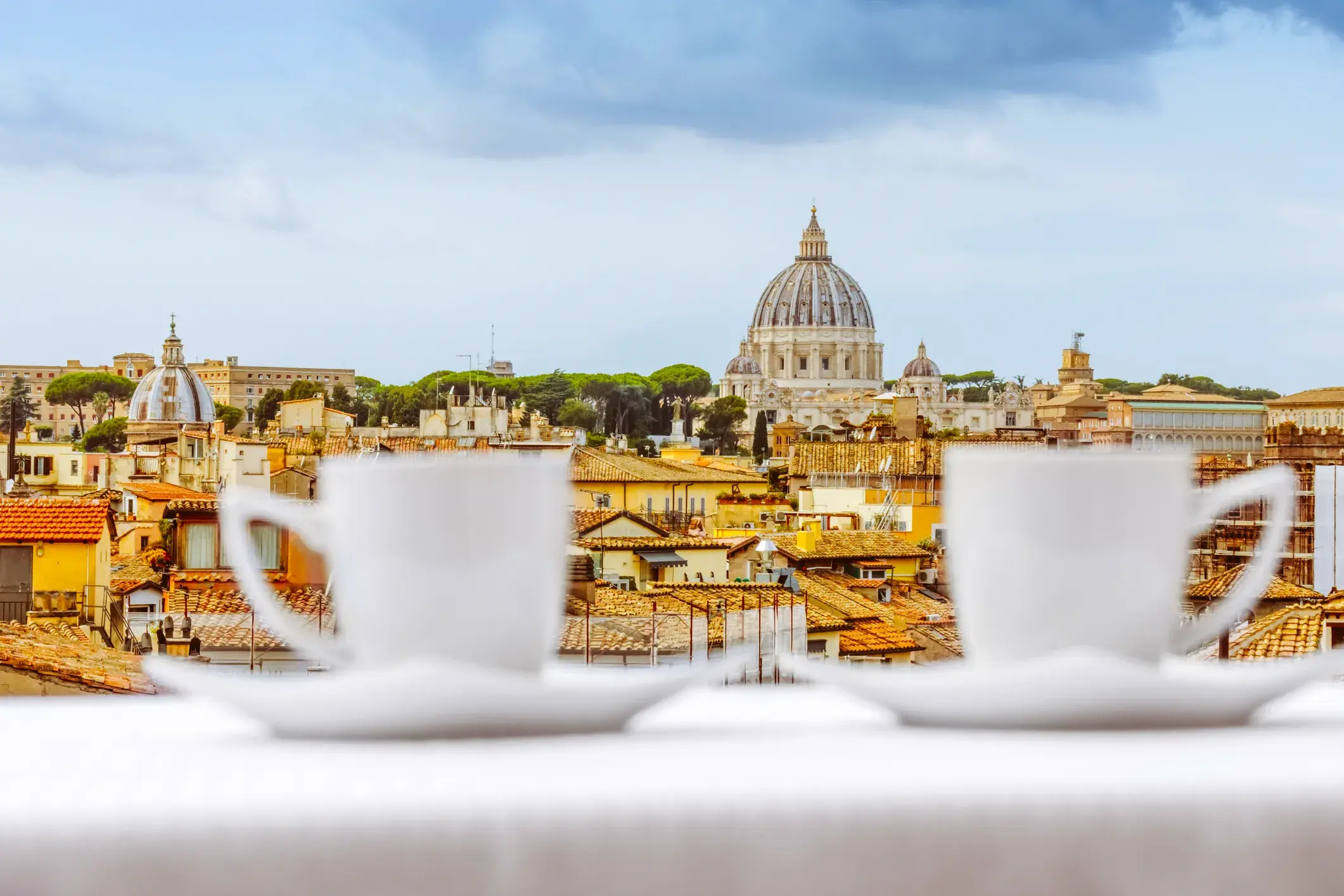 Zwei weiße Kaffeetassen auf einem Tisch mit Blick über die Dächer von Rom auf die Kuppel der Peterskirche im Vatikan.