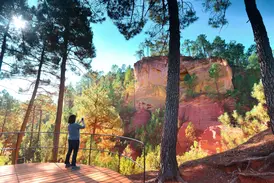 Eine Frau fotografiert von einer Holzplattform die leuchtenden Ockerfelsen von Roussillon im Naturpark Luberon.