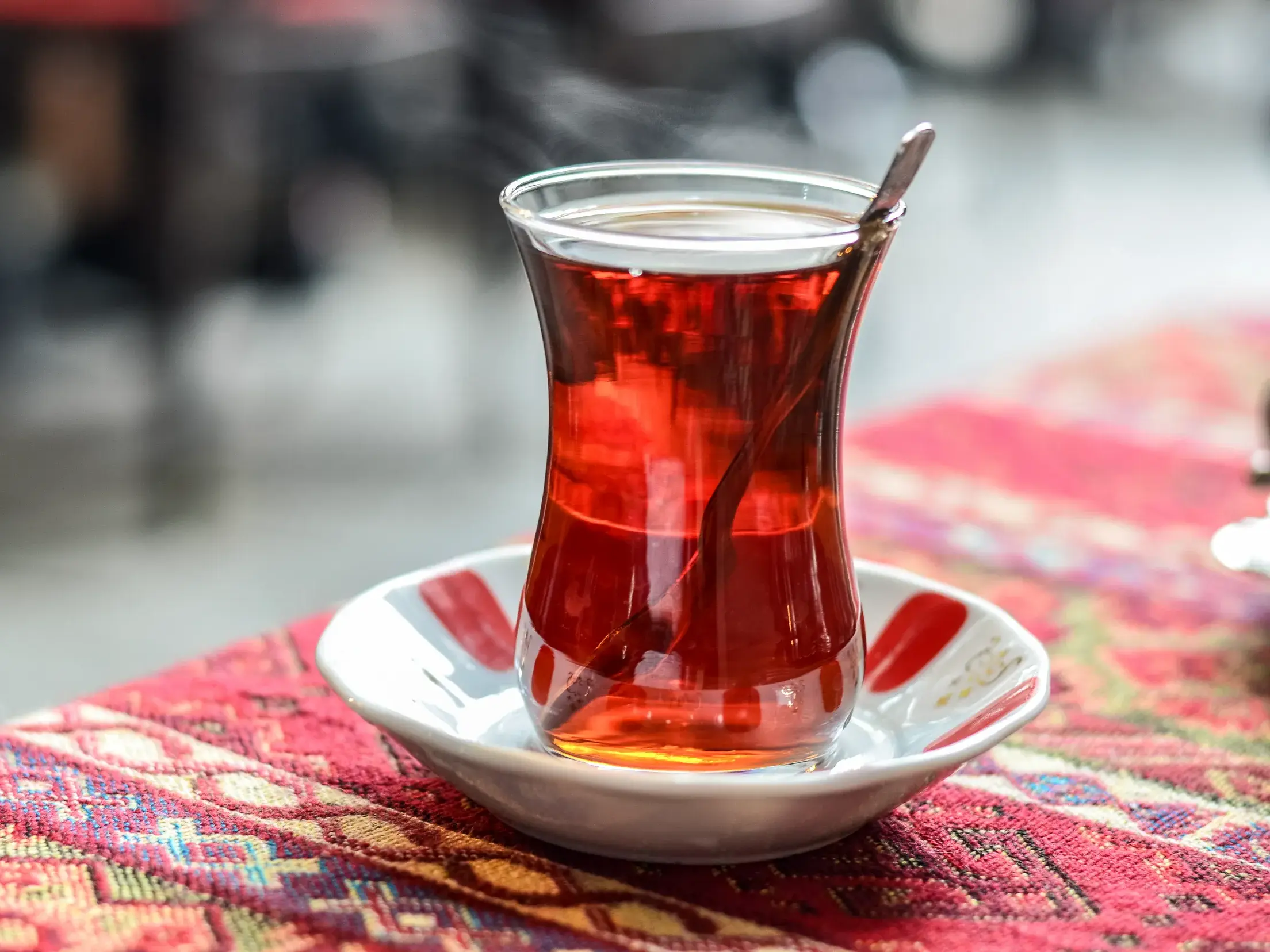 Dampfender türkischer Tee in einem tulpenförmigen Glas auf einem bunten Tischtuch, Symbol der Gastfreundschaft in Anatolien.