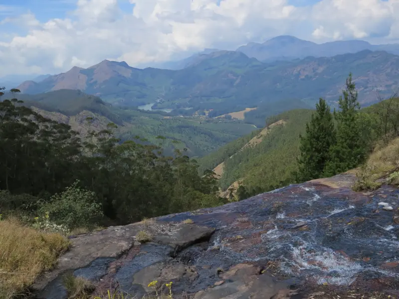 Panoramablick beim Trekking in den Western Ghats: Ein Gebirgsbach fließt über Felsen mit Aussicht auf bewaldete Täler Keralas.