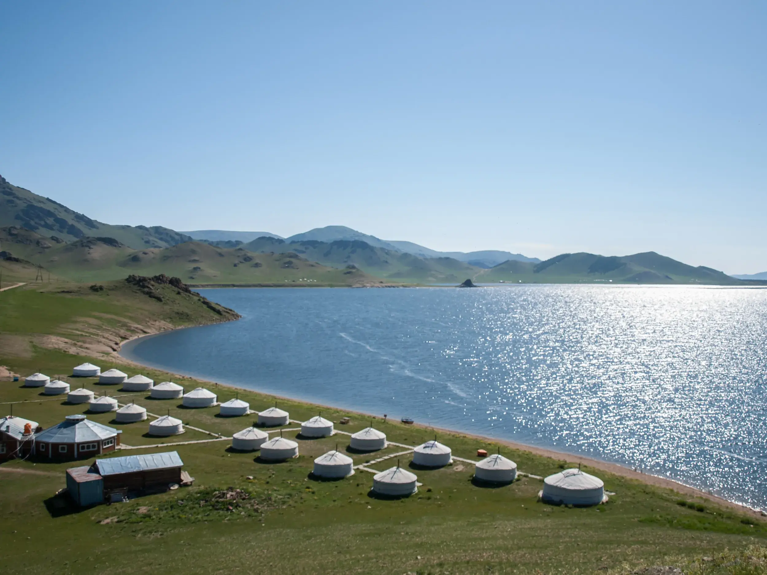 Traditionelles Jurtenlager direkt am Ufer des glitzernden Terkhiin Tsagaan-Sees in der weiten Steppenlandschaft der Mongolei.