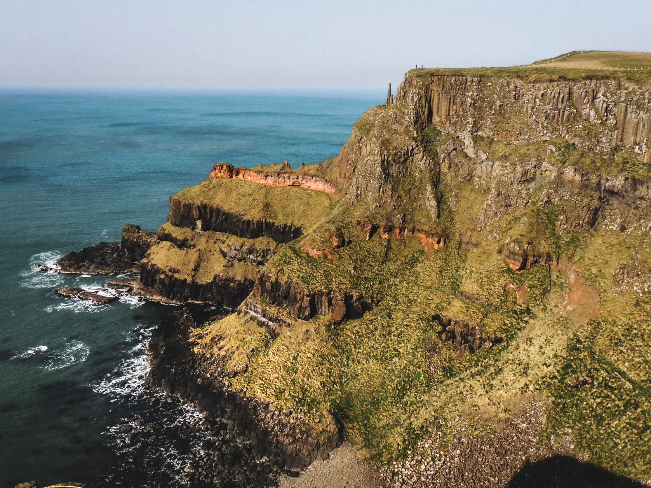 Wanderer auf den dramatischen, grün bewachsenen Klippen des Fair Head mit weitem Blick über die raue Küste und die Sea of Moyle.