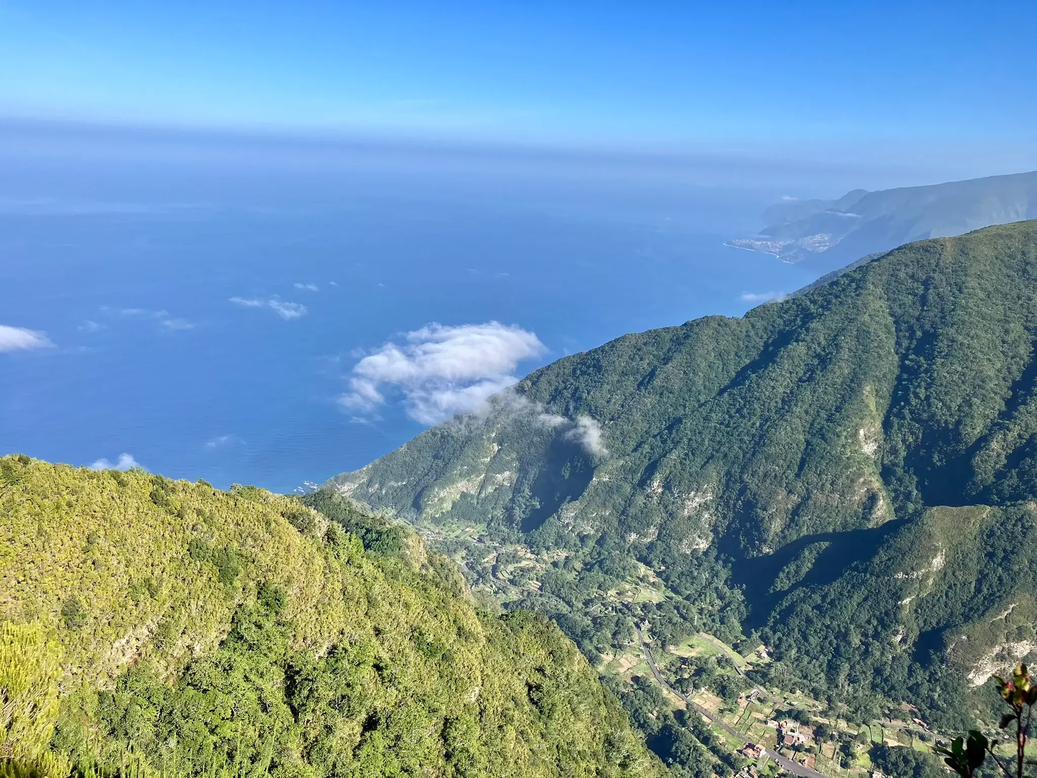 Aussicht beim Wandern auf Madeira über dicht bewachsene Berghänge und ein Tal hinweg auf den weiten Atlantischen Ozean.
