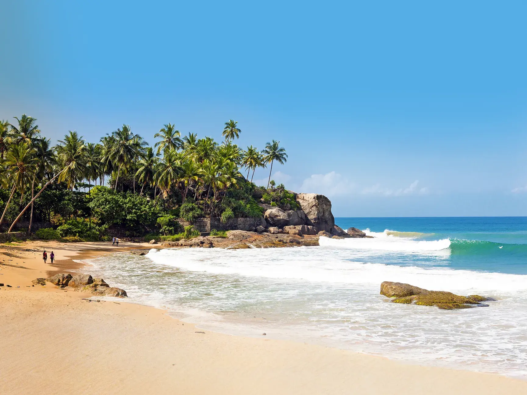 Idyllischer Sandstrand in Mirissa, Sri Lanka, mit einer palmengesäumten Felsklippe am türkisfarbenen Indischen Ozean.