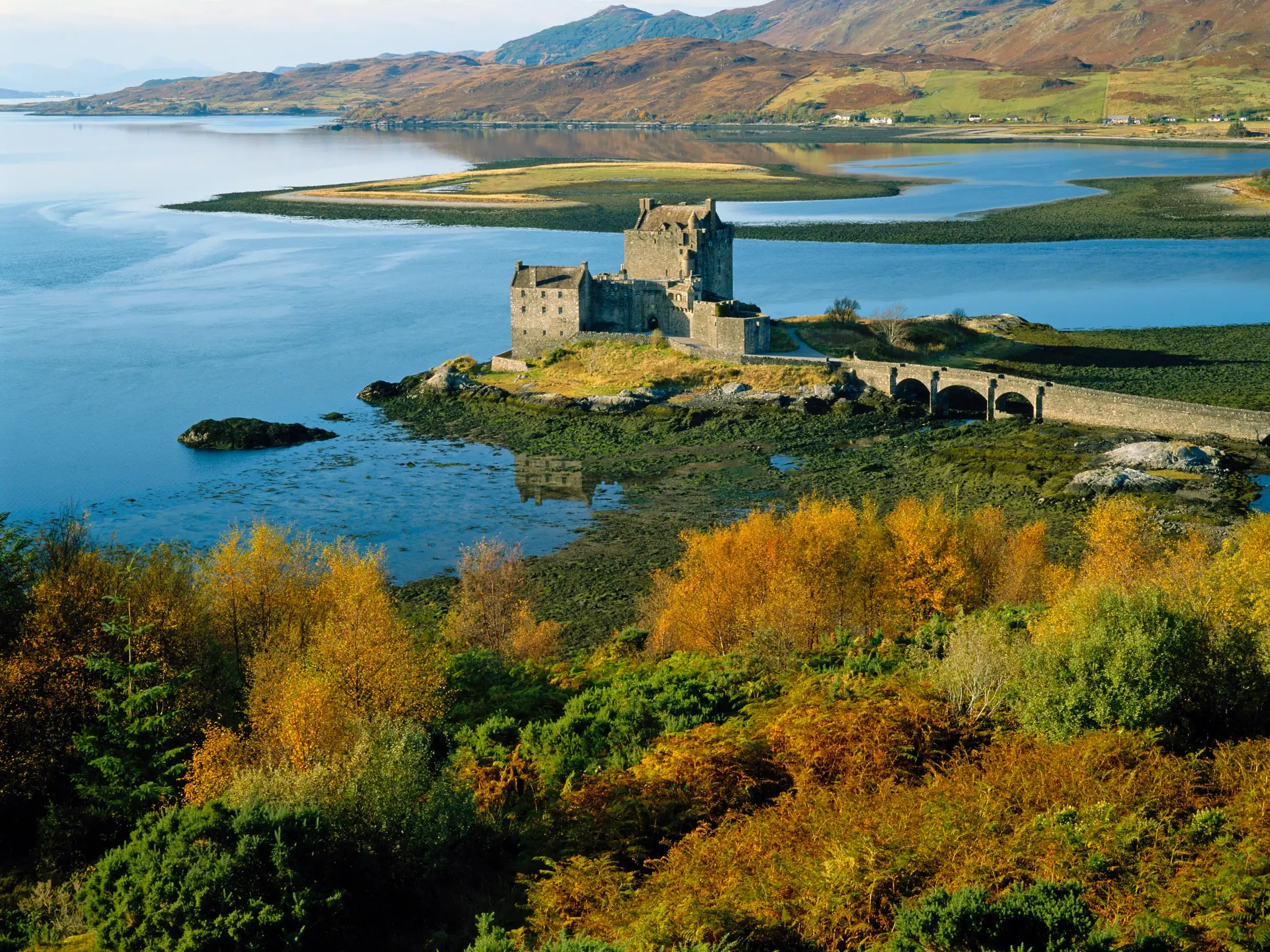 Das berühmte Eilean Donan Castle in den Highlands, über eine Steinbrücke erreichbar, umgeben von herbstlicher Natur Schottlands.
