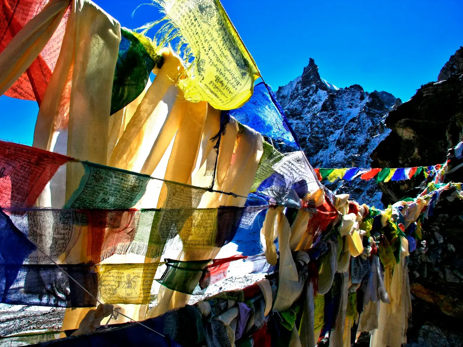 Bunte Gebetsfahnen flattern im Wind vor der Kulisse eines schneebedeckten Gipfels im nepalesischen Himalaya.