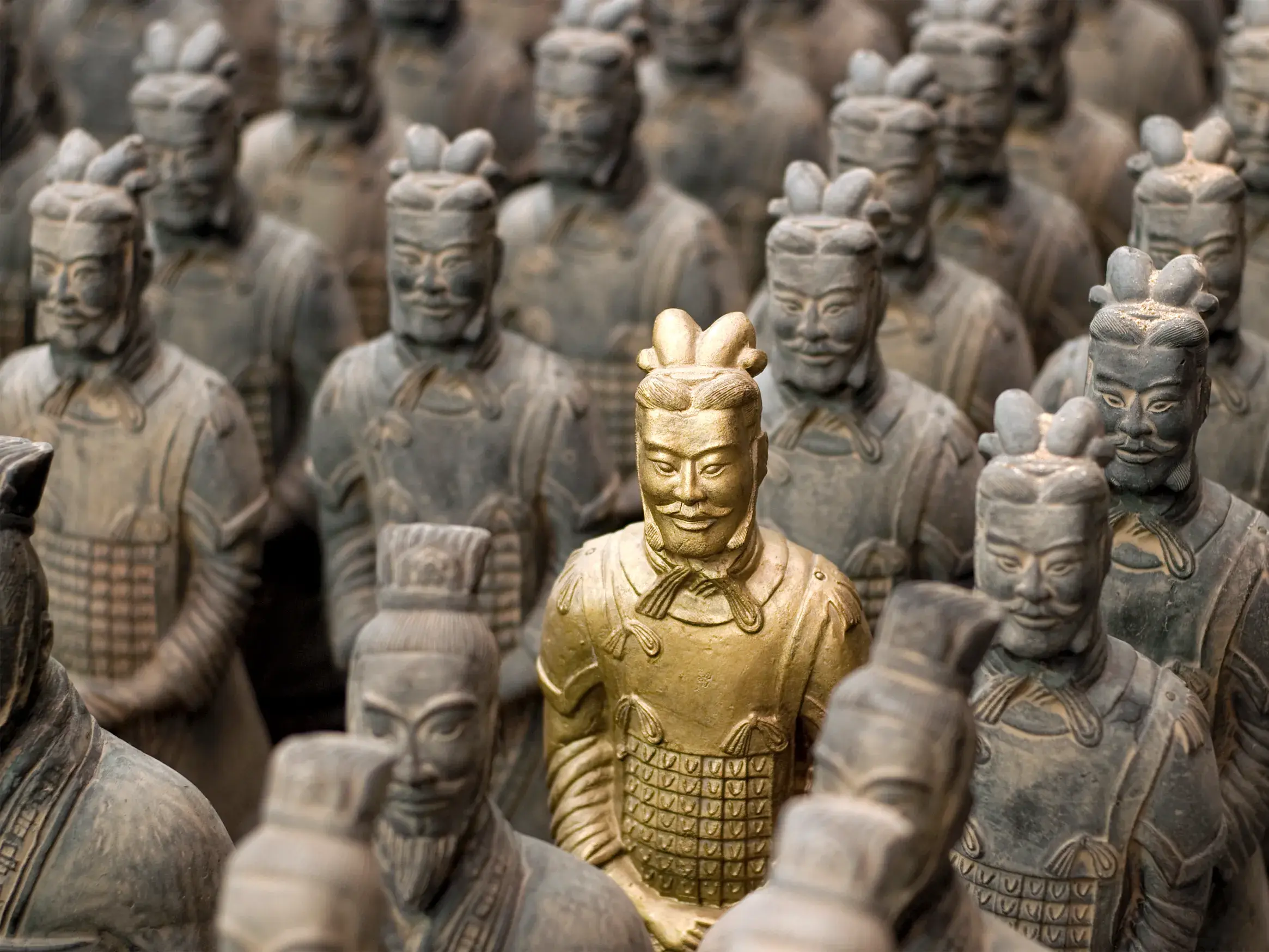 Nahaufnahme der berühmten Terrakotta-Armee in Xian mit einem goldenen Krieger im Fokus umgeben von grauen Tonsoldaten.