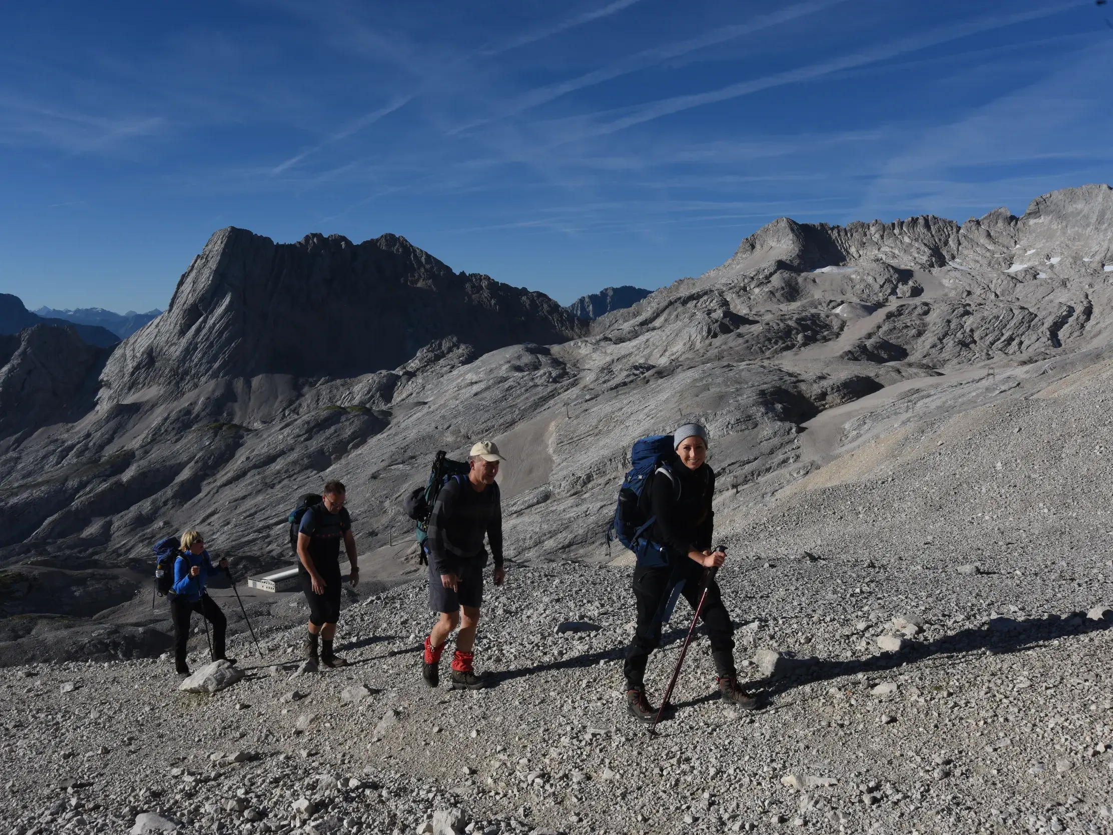Eine Wandergruppe steigt bei Sonnenschein über den geröllreichen Weg am Zugspitzplatt in Richtung Gipfel der Zugspitze auf.