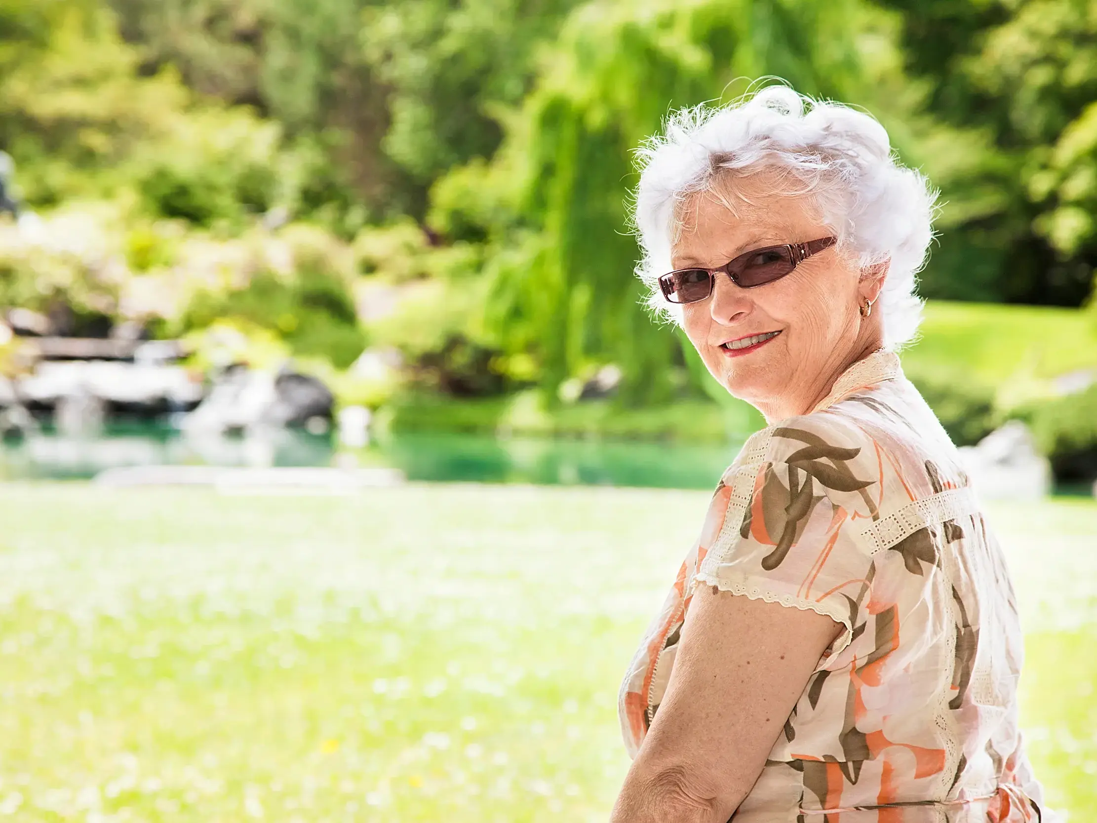 Eine Seniorin genießt auf einer Studiosus Studienreise einen entspannten Moment in einem sonnigen, grünen Garten in Schottland.