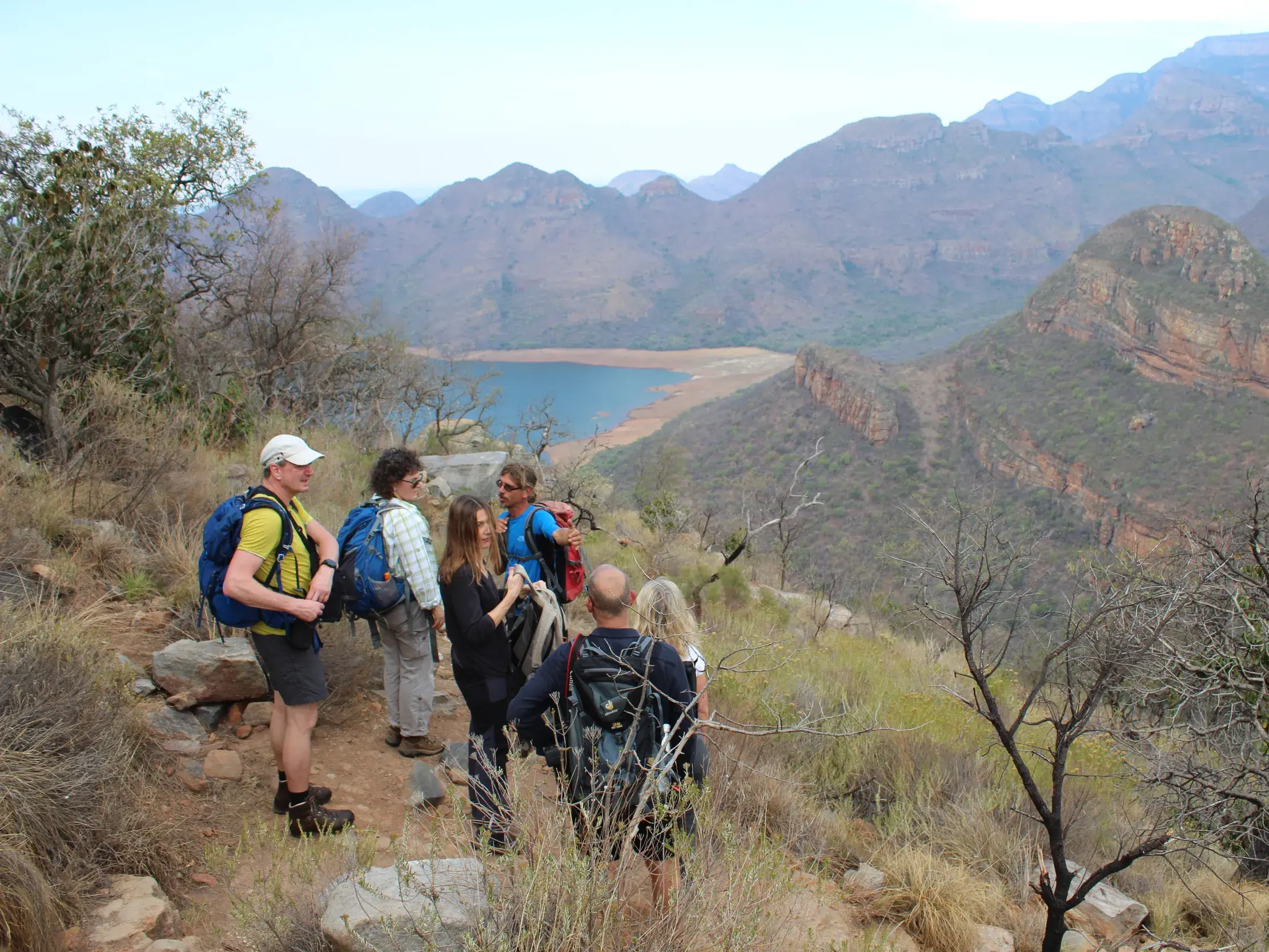 Eine Reisegruppe mit Rucksäcken macht eine Wanderpause mit Panoramablick über den gewaltigen Blyde River Canyon in Südafrika.