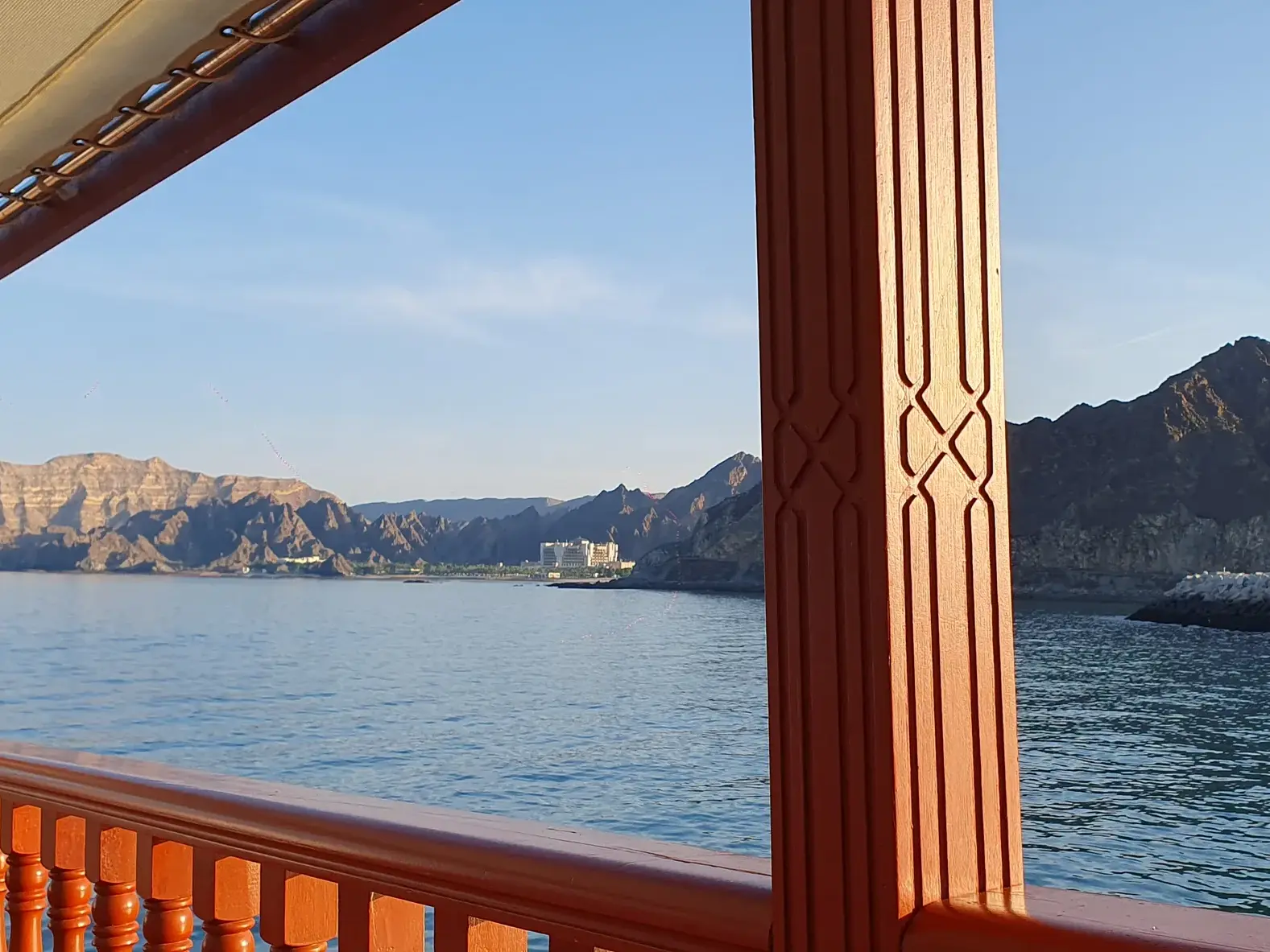 Blick von einer traditionellen hölzernen Dhau auf das Meer und die bergige Küstenlandschaft von Maskat im Oman bei Sonnenuntergang.