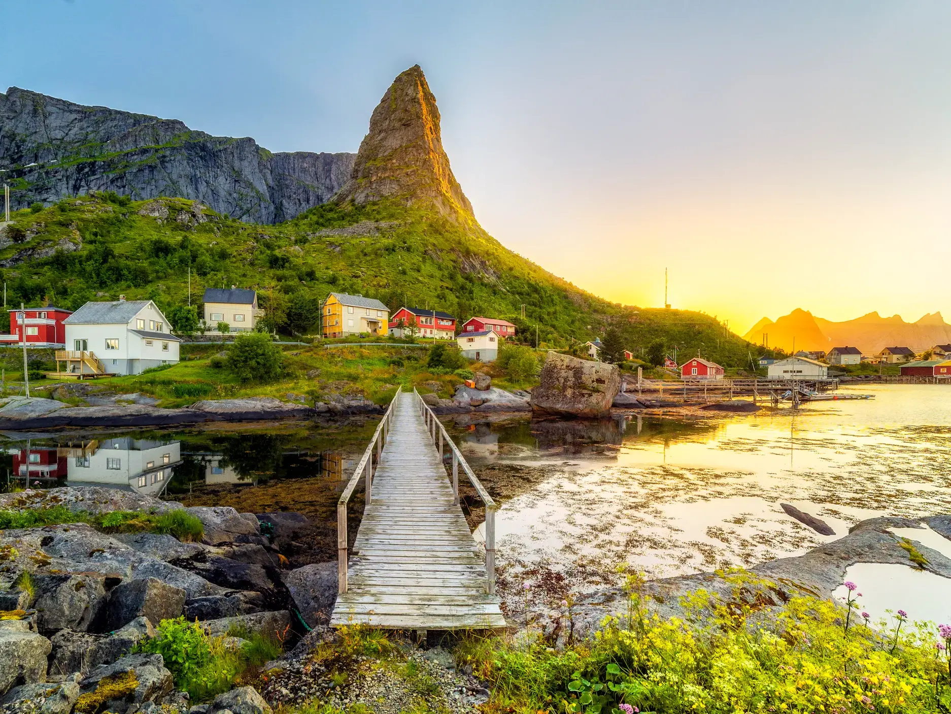 Malerisches Fischerdorf Reine auf den Lofoten mit bunten Holzhäusern vor dem markanten Olstind-Berg im warmen Abendlicht.