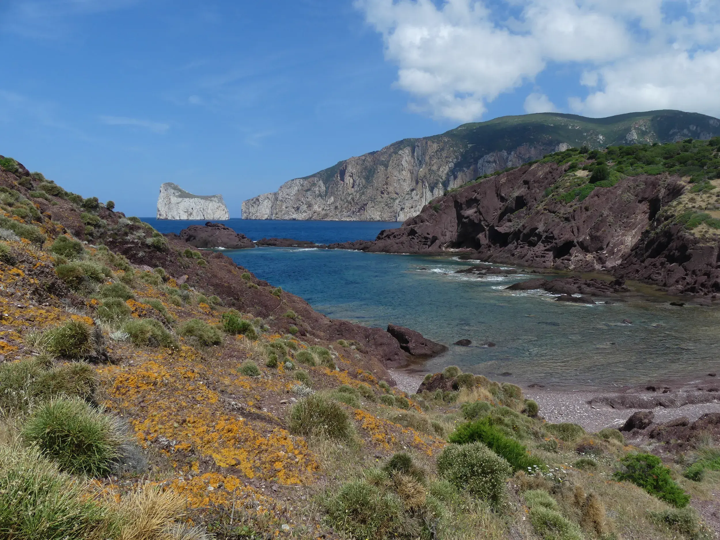 Panoramablick bei einer Wanderung an der Küste von Masua auf den Felsen Pan di Zucchero und das tiefblaue Meer Sardiniens.