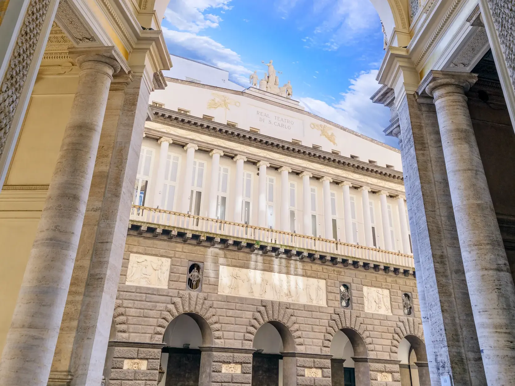 Architektonischer Blick durch die Säulen des Palazzo Reale auf die prachtvolle Fassade des Teatro San Carlo in Neapel.