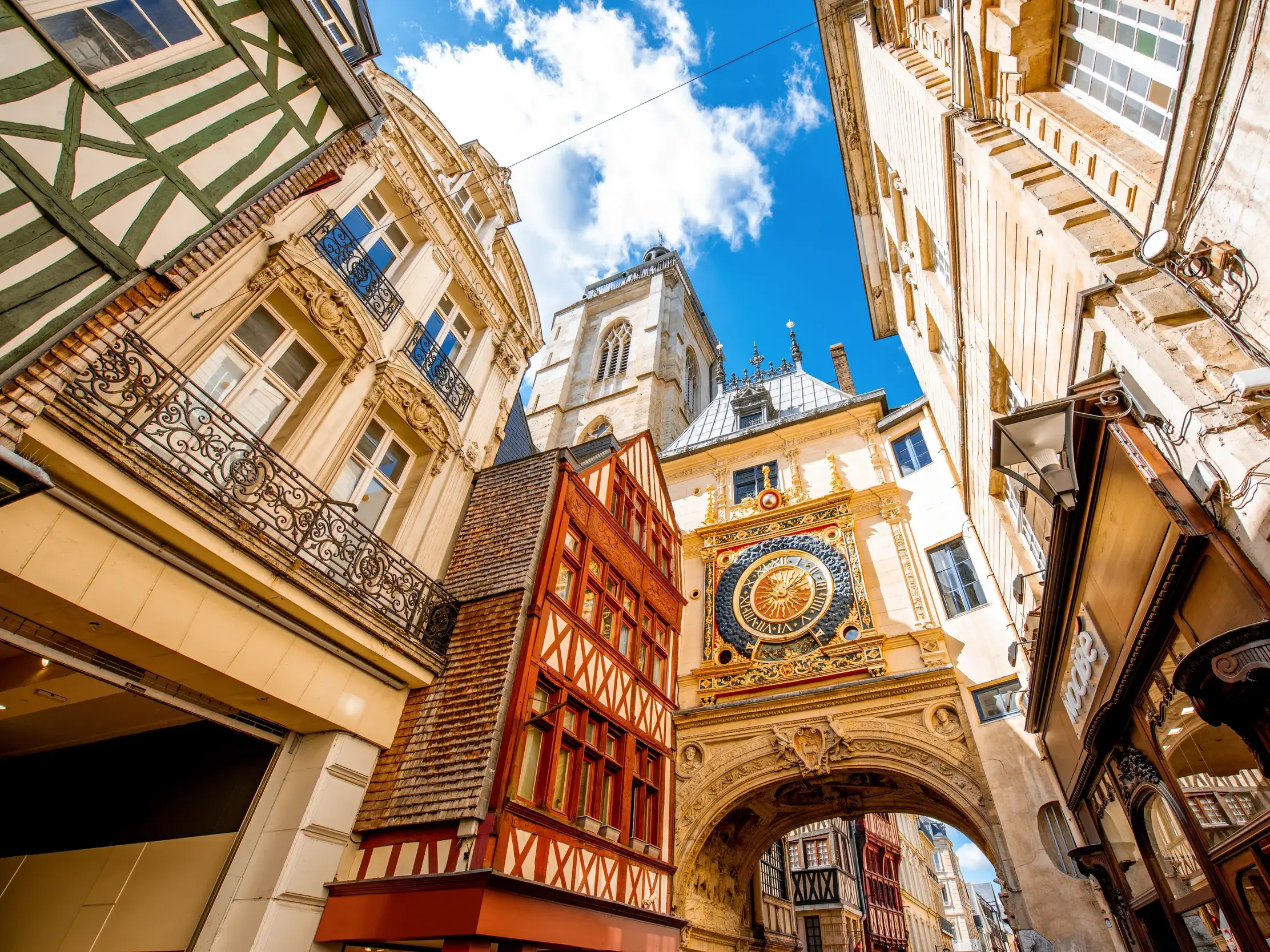 Blick von unten auf eine gold-blaue astronomische Uhr und die historischen Fachwerkhäuser in der Altstadt von Rouen.