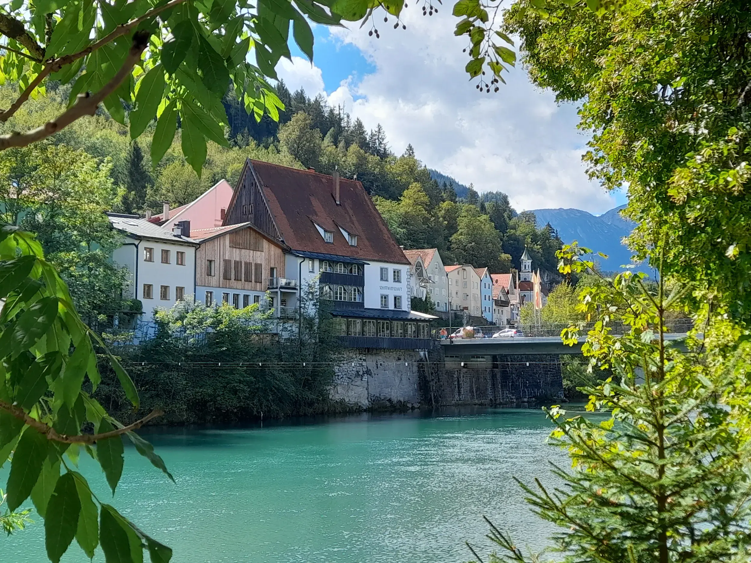 Malerischer Blick vom Lechfall auf die Altstadt von Füssen am türkisfarbenen Lech vor der Kulisse der Ammergauer Alpen.