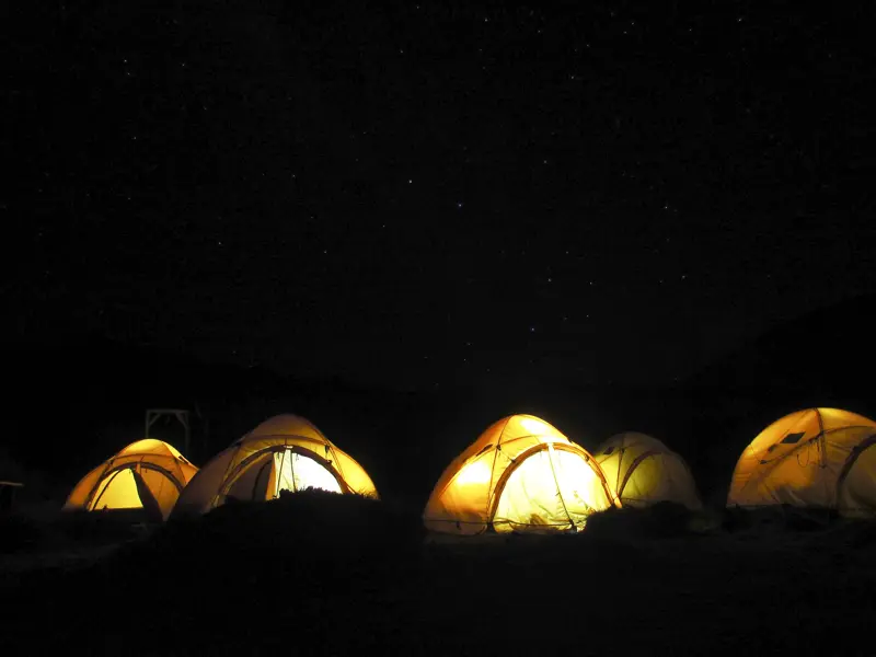 Ein Zeltlager mit gelb leuchtenden Zelten unter dem Sternenhimmel bei einer Trekking-Tour am Kilimanjaro.