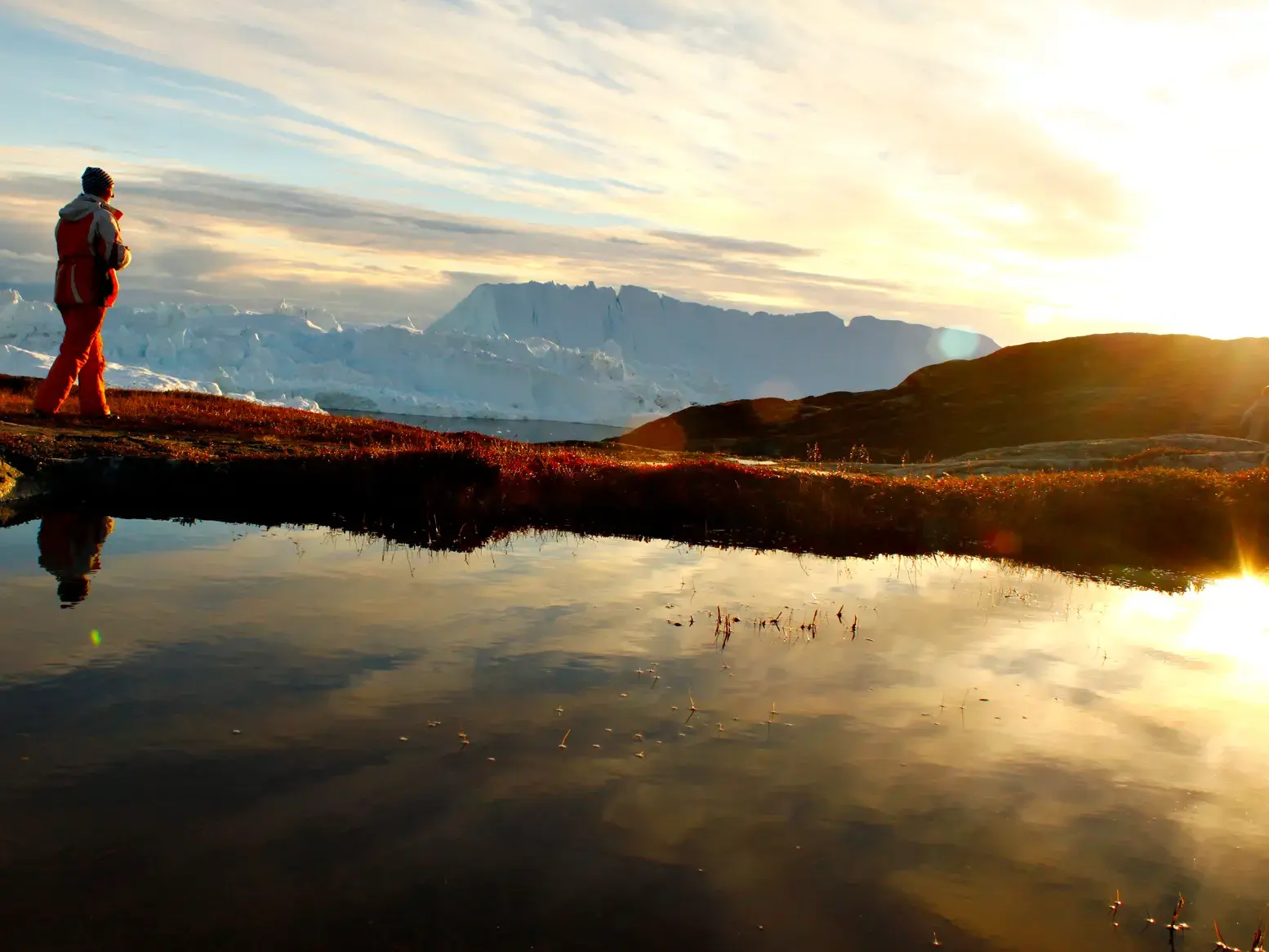 Wanderer in der Abendsonne am Ufer eines Sees mit Blick auf die riesigen Gletscher des Ilulissat-Eisfjords in Grönland.