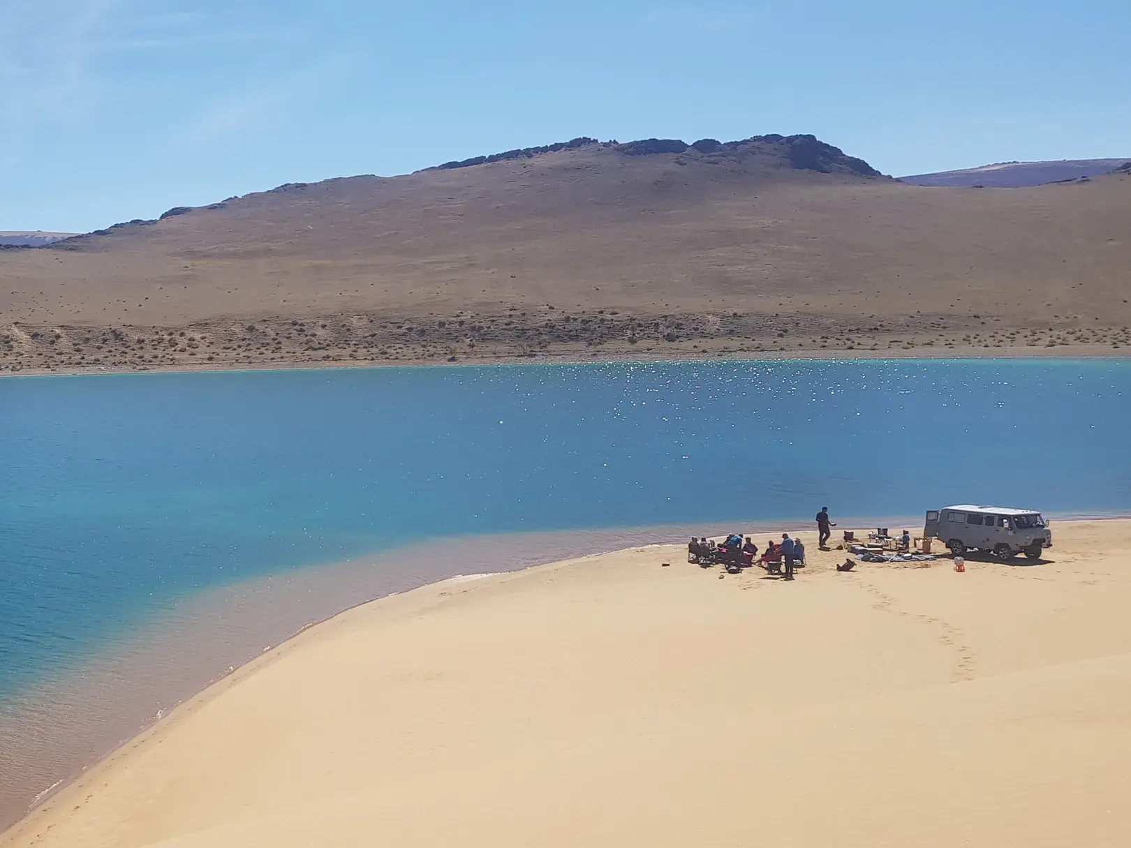 Eine Trekkinggruppe pausiert mit ihrem Kleinbus am Sandufer des malerischen Khar-Sees in der weiten Steppe der Mongolei.