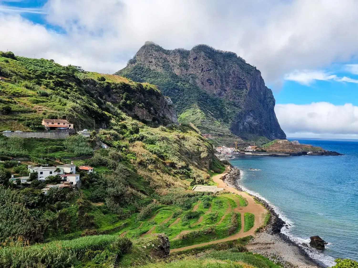 Grüne, terrassierte Steilküste nahe Porto da Cruz auf Madeira, überragt von einem massiven Felsen am tiefblauen Atlantik.