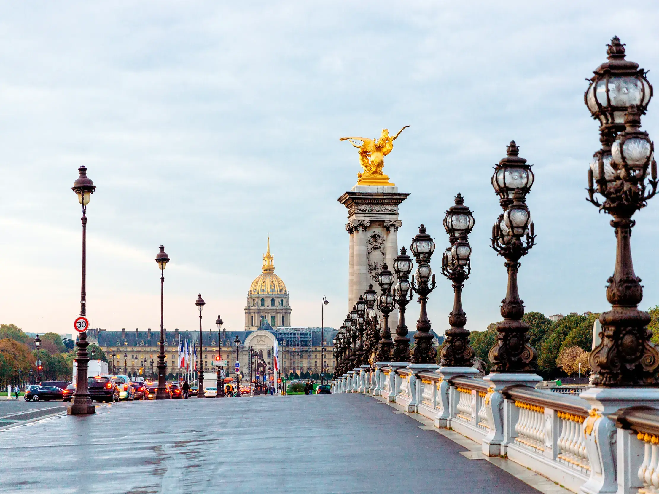 Die prunkvolle Brücke Pont Alexandre III über die Seine in Paris mit verzierten Laternen und der goldenen Kuppel des Invalidendoms im Hintergrund.
