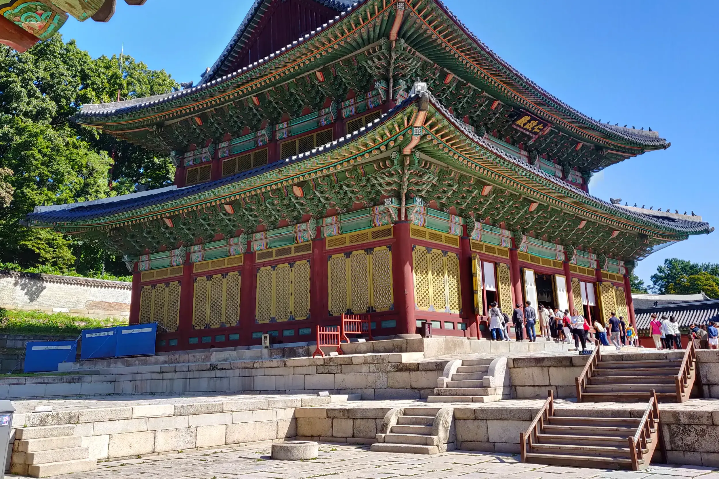 Reisegruppe vor der reich verzierten Haupthalle des Changdeokgung-Palastes in Seoul unter blauem Himmel