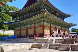 Reisegruppe vor der reich verzierten Haupthalle des Changdeokgung-Palastes in Seoul unter blauem Himmel