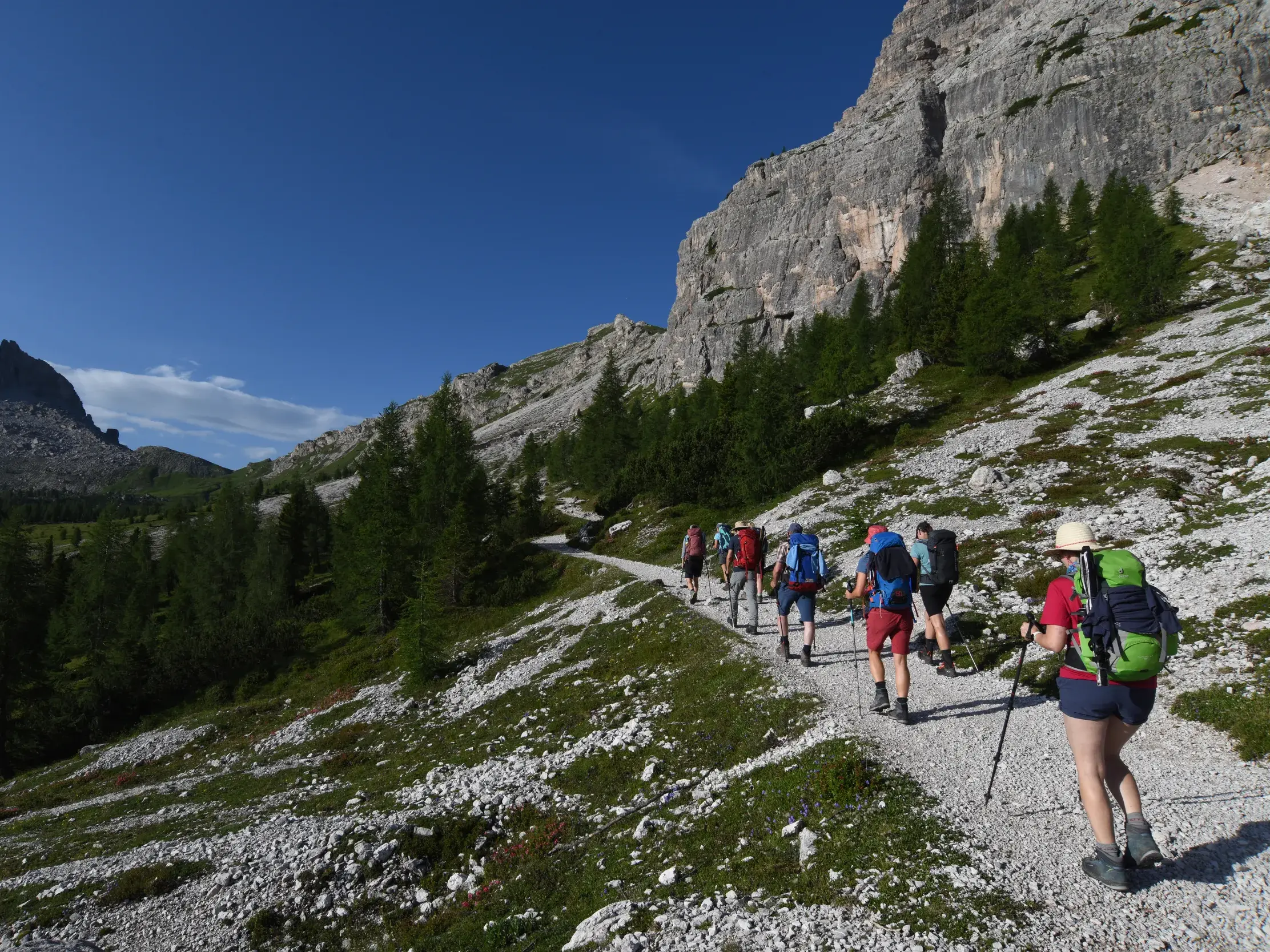 Eine Trekkinggruppe wandert auf dem Dolomiten-Höhenweg Alta Via 1 entlang einer Felswand mit Blick auf einen markanten Gipfel.