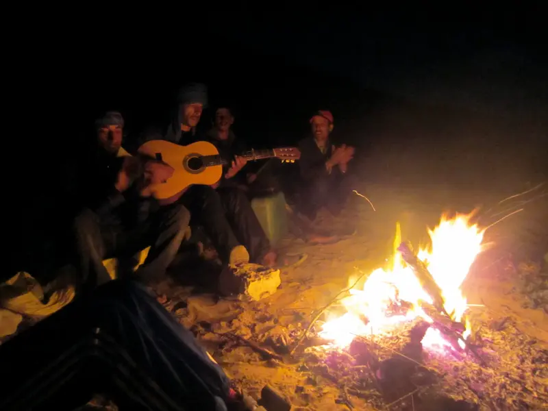 Eine Hauser-Reisegruppe lauscht bei einem Kamel-Trekking in Marokko am prasselnden Lagerfeuer den Klängen einer Gitarre.