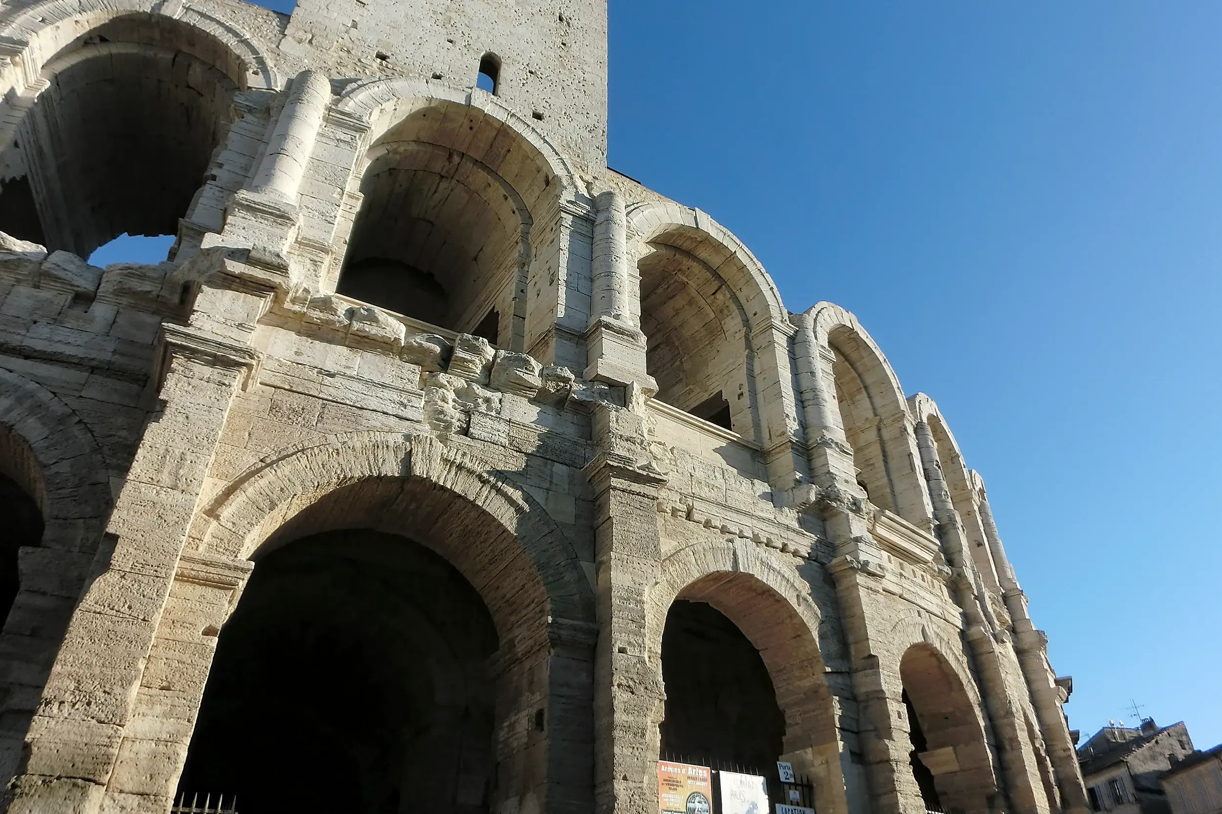 Die historischen Steinbögen der römischen Arena in Arles (UNESCO-Welterbe) unter dem strahlend blauen Himmel der Provence.
