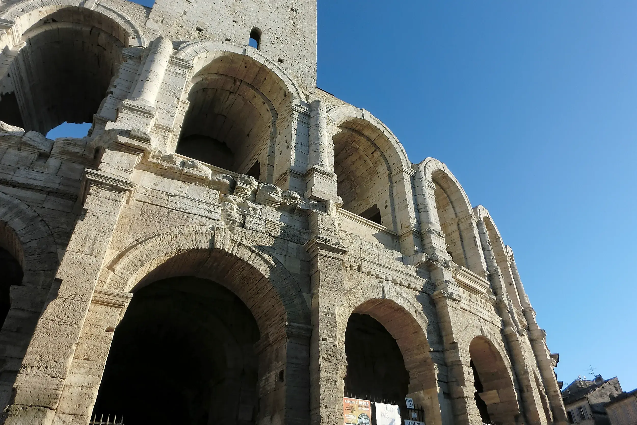 Die historischen Steinbögen der römischen Arena in Arles (UNESCO-Welterbe) unter dem strahlend blauen Himmel der Provence.