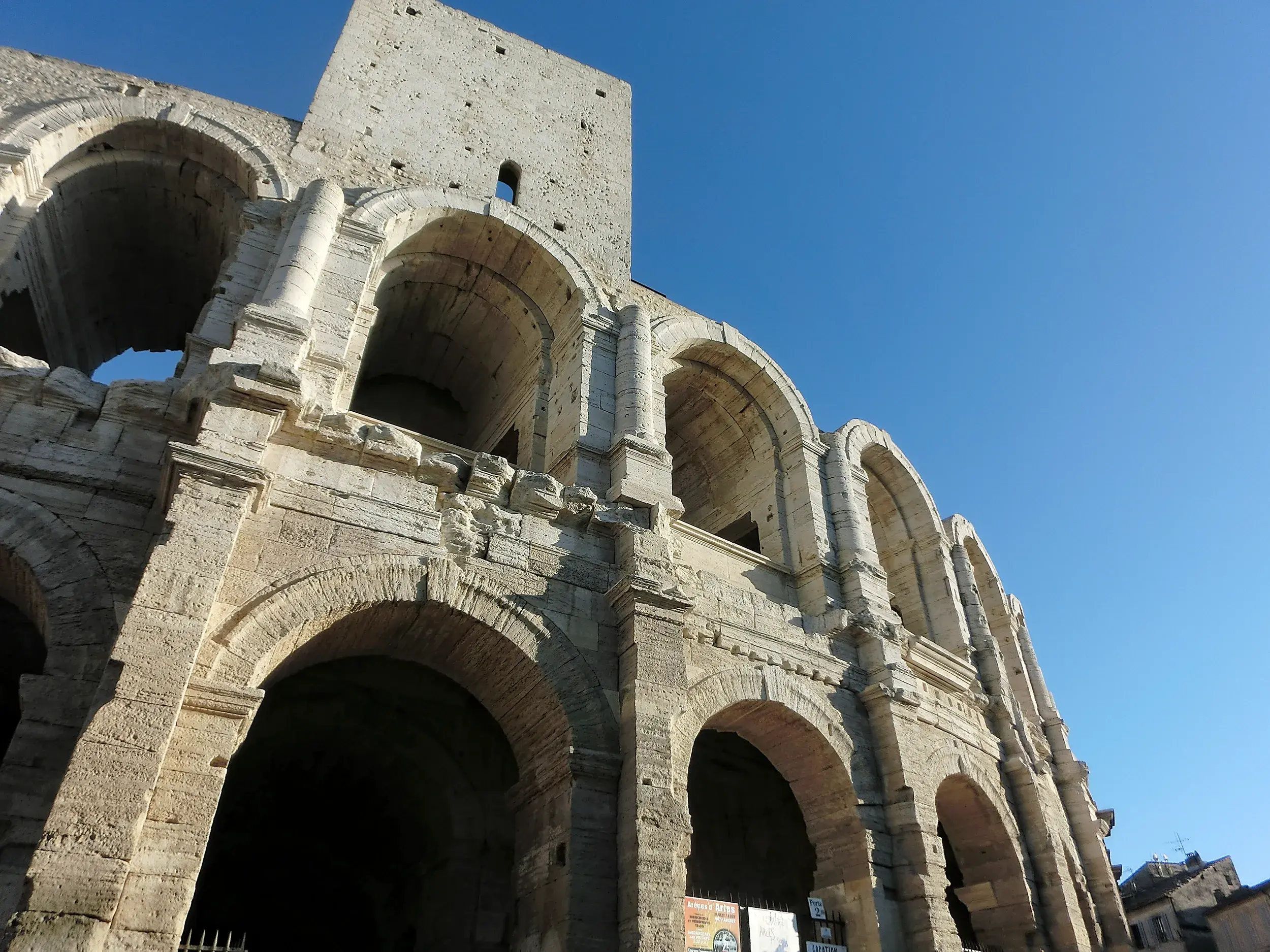 Die historischen Steinbögen der römischen Arena in Arles (UNESCO-Welterbe) unter dem strahlend blauen Himmel der Provence.