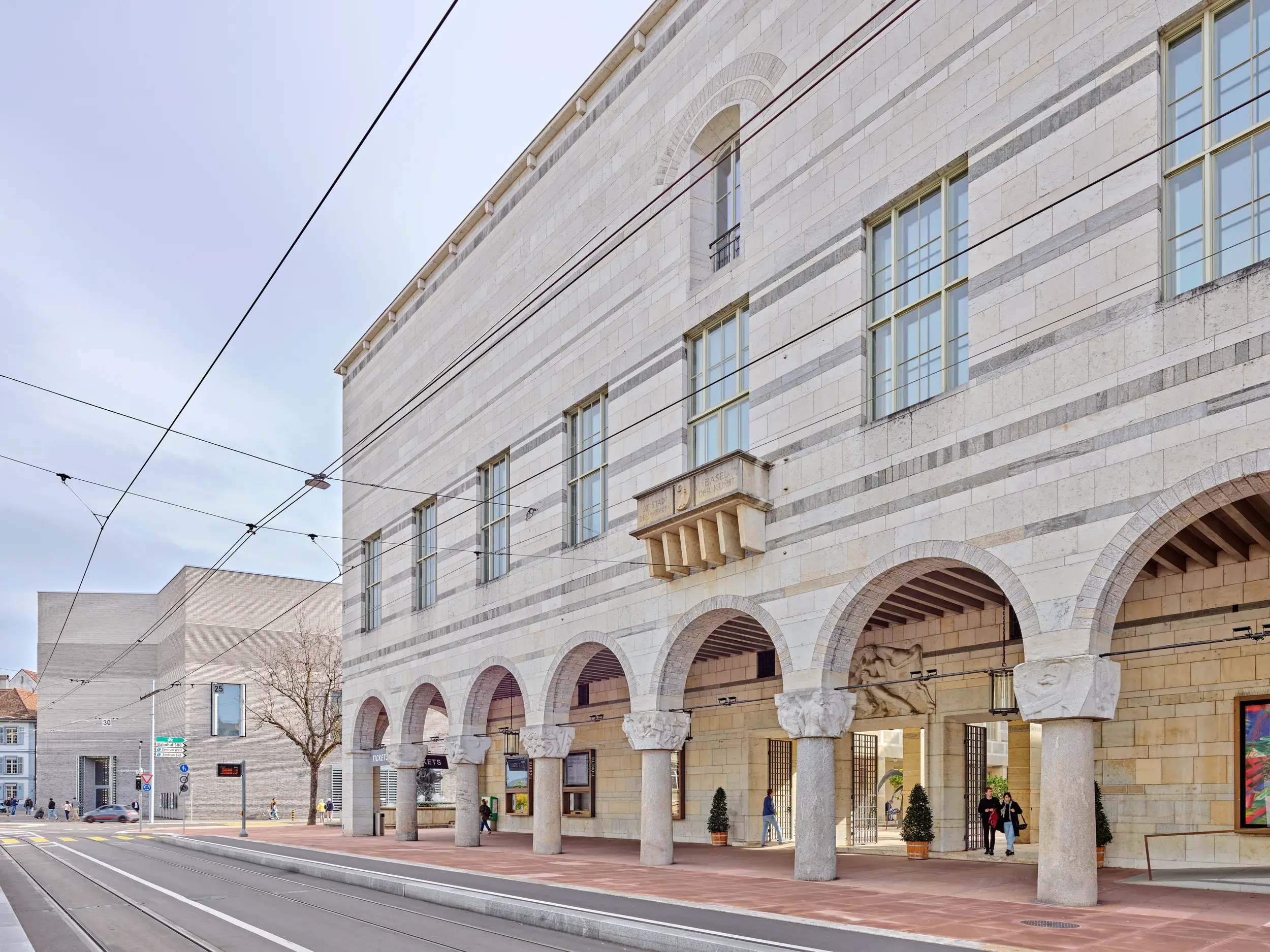 Fassade mit Arkaden des Kunstmuseum Basel an einer Straße mit Straßenbahnschienen