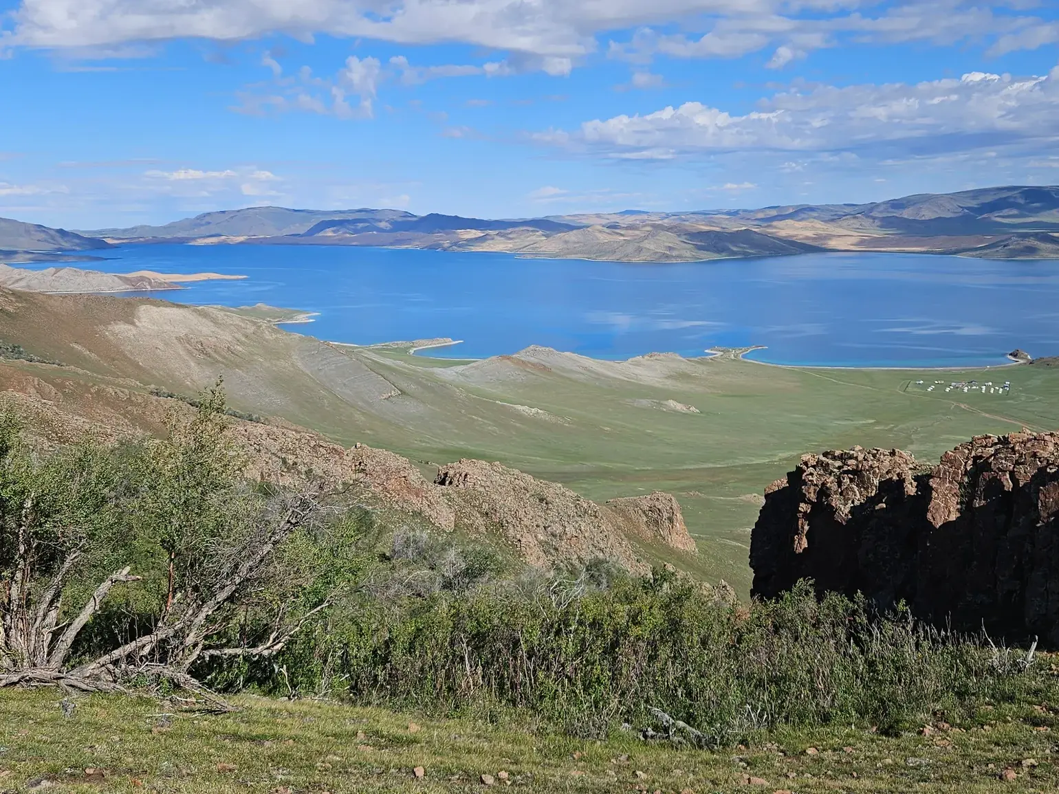 Panoramablick während einer Wanderung in der Mongolei über den tiefblauen See Khar Nuur und die weite Steppenlandschaft.