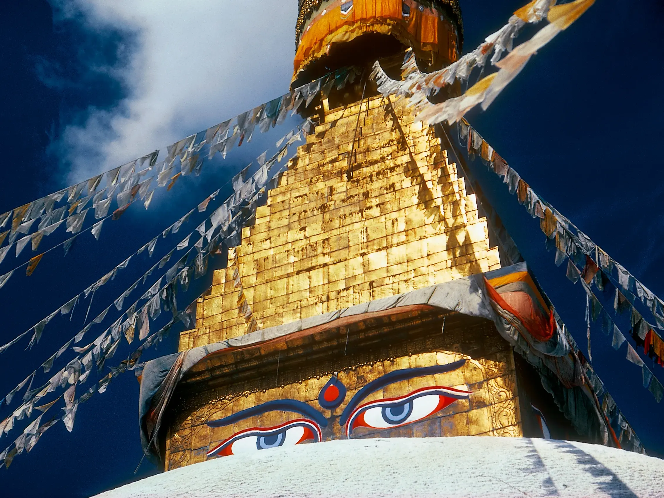 Nahaufnahme der goldenen Spitze des Bodnath-Stupa in Kathmandu mit den Augen des Buddha und flatternden Gebetsfahnen.