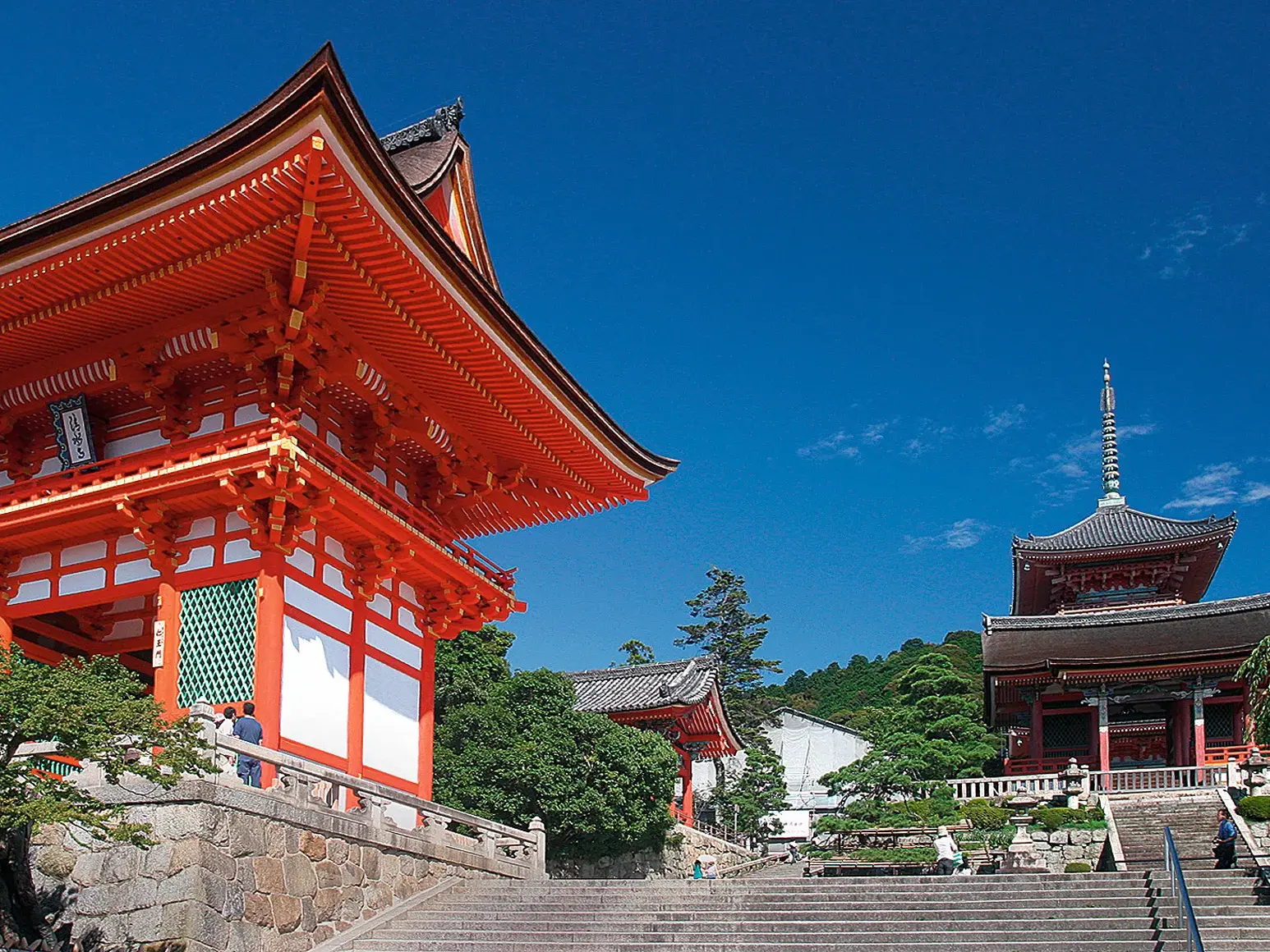 Aufstieg zum berühmten Kiyomizu-dera Tempel in Kyoto mit seiner leuchtend roten Pagode vor einem strahlend blauen Himmel.