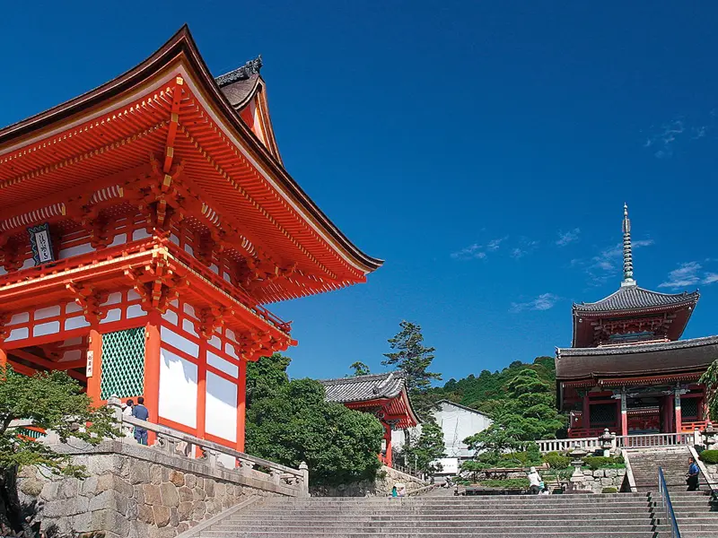 Aufstieg zum berühmten Kiyomizu-dera Tempel in Kyoto mit seiner leuchtend roten Pagode vor einem strahlend blauen Himmel.