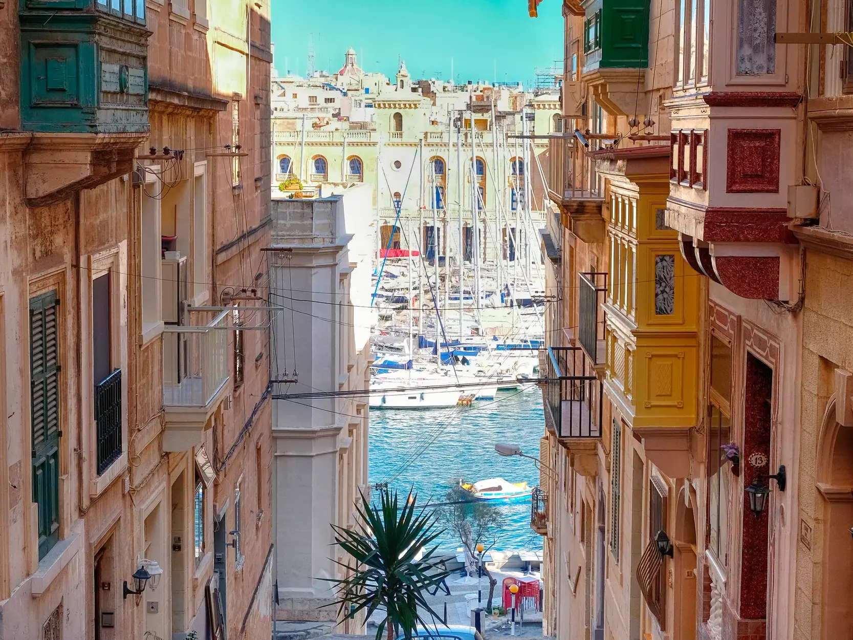 Blick durch eine enge Gasse in Valletta mit traditionellen bunten Balkonen auf den Hafen und die Drei Städten.