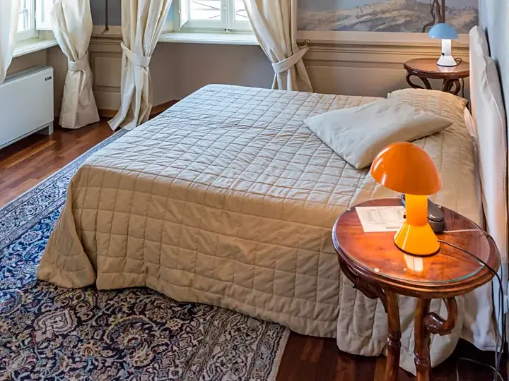Doppelbett mit beiger Steppdecke in einem romantischen Zimmer des Hotels Alla Corte degli Angeli in der Altstadt von Lucca.