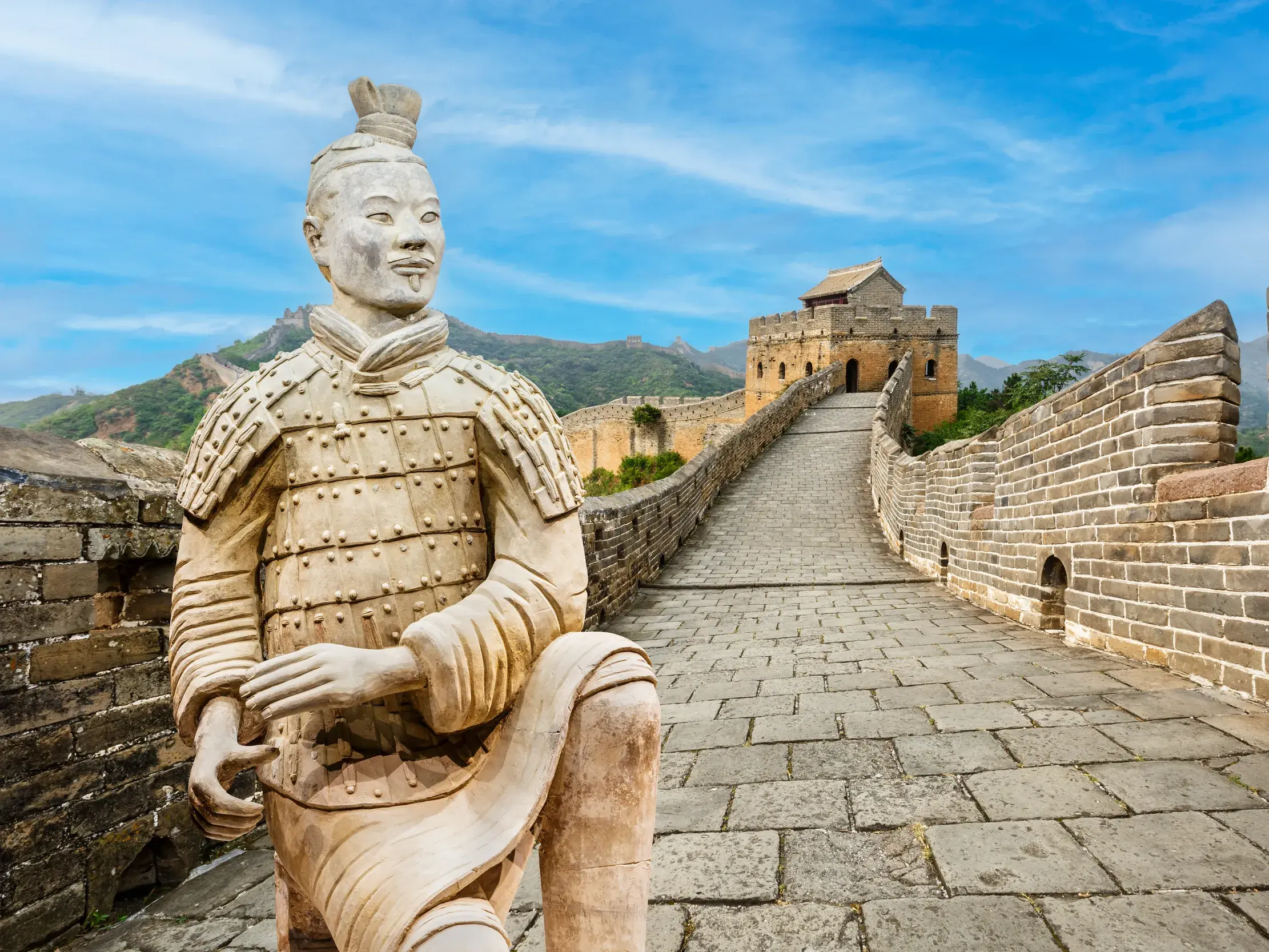 Ein Terrakotta-Soldat aus Xian vor der Großen Mauer, zwei Höhepunkte einer China-Studienreise bei sonnigem Wetter.