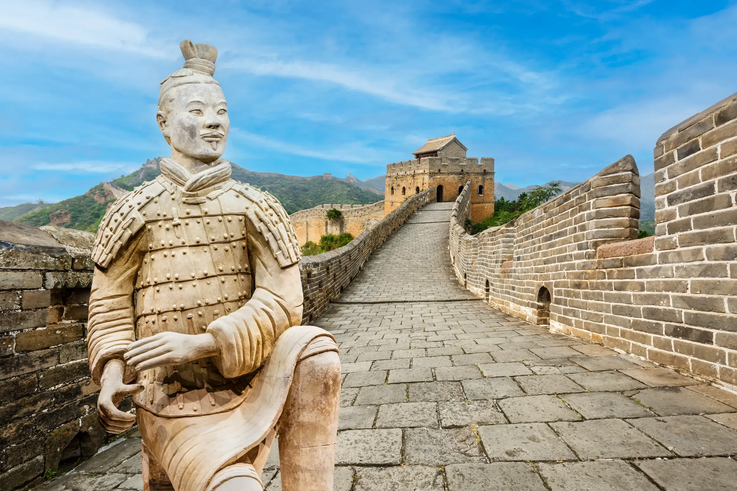 Ein Terrakotta-Soldat aus Xian vor der Großen Mauer, zwei Höhepunkte einer China-Studienreise bei sonnigem Wetter.