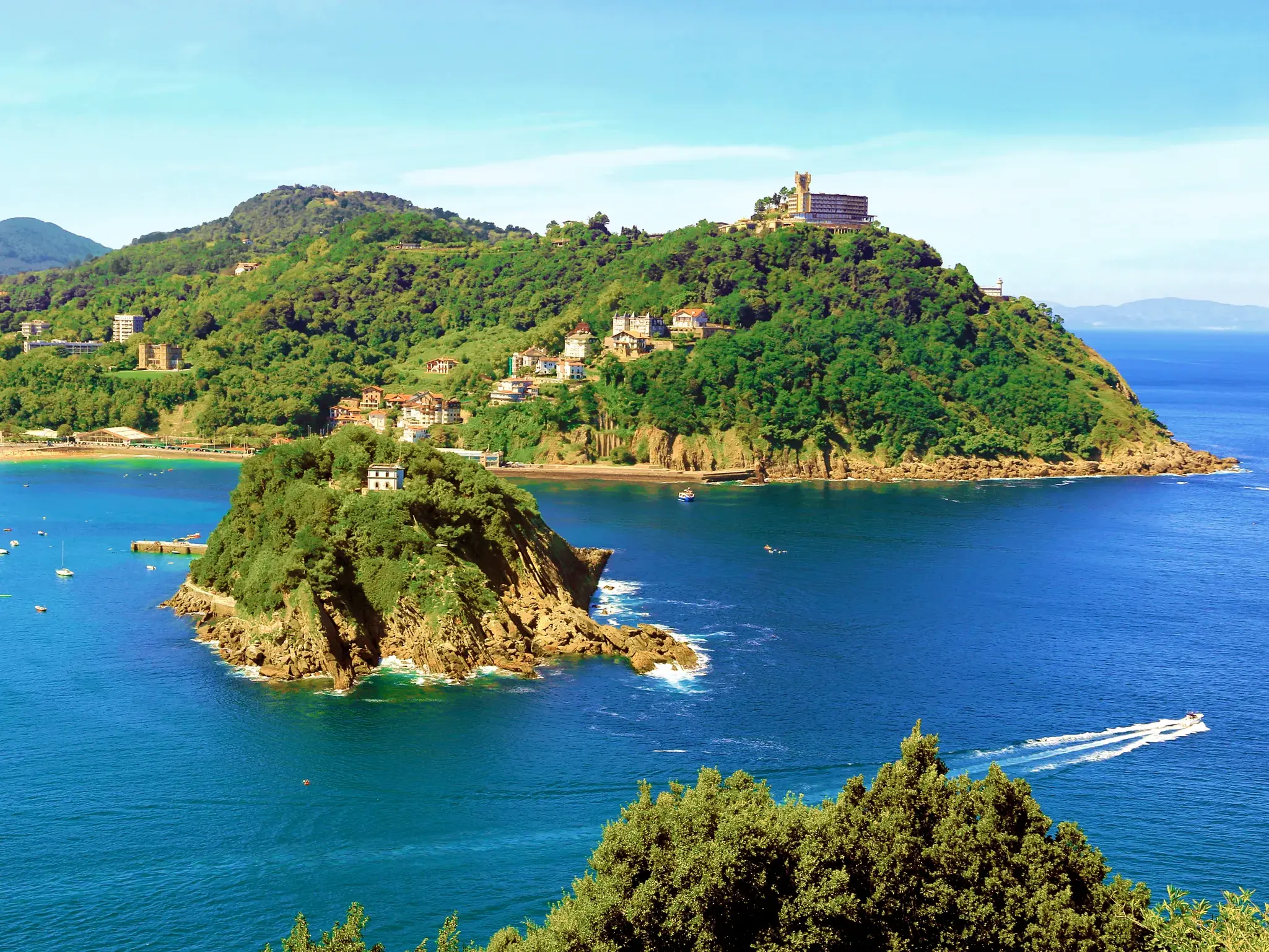 Sonniger Panoramablick auf die Muschelbucht La Concha in San Sebastián mit der Insel Santa Clara und grünen Hügeln.
