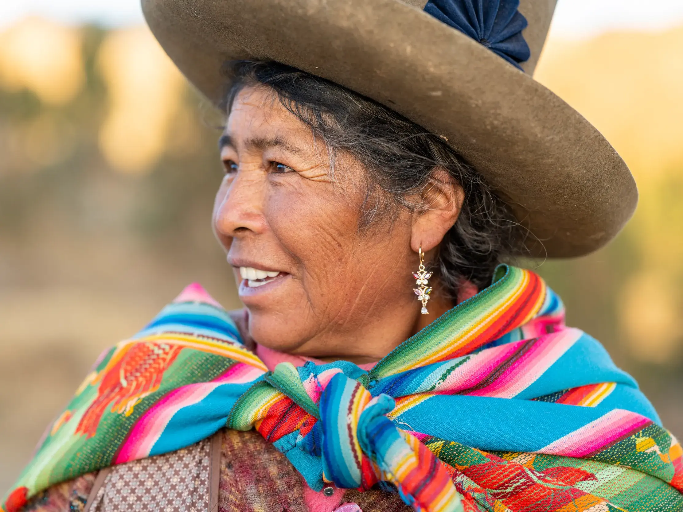 Herzliche Begegnung in den Anden: eine einheimische Frau in Peru mit traditionellem Hut und buntem Tuch lächelt freundlich.