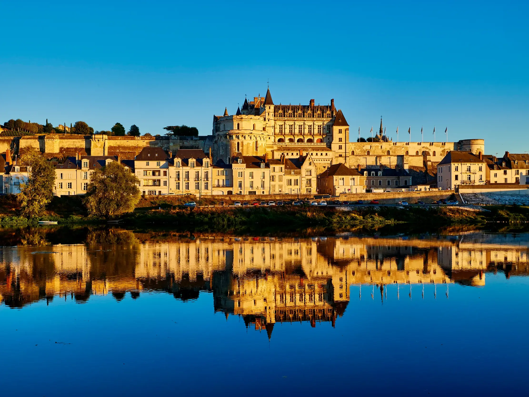 Das majestätische Schloss Amboise und die Stadt im goldenen Morgenlicht, gespiegelt in der ruhigen Loire.