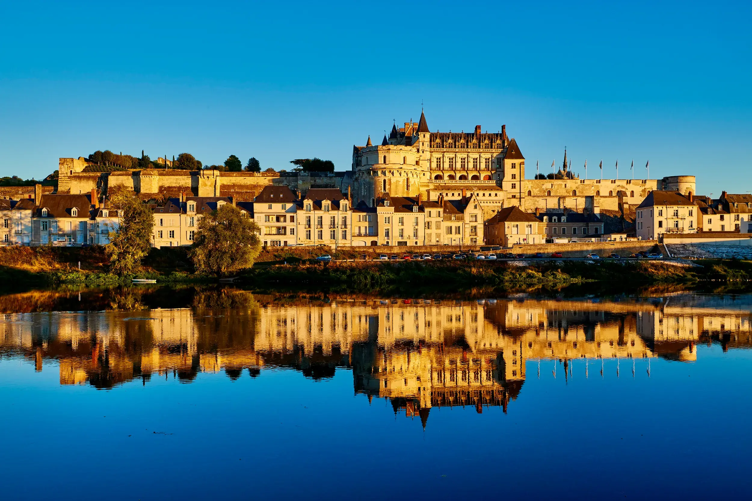 Das majestätische Schloss Amboise und die Stadt im goldenen Morgenlicht, gespiegelt in der ruhigen Loire.