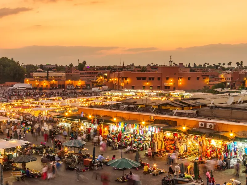 Abenddämmerung über dem belebten Marktplatz Djemaa el-Fna in Marrakesch mit vielen Menschen und hell erleuchteten Souks.